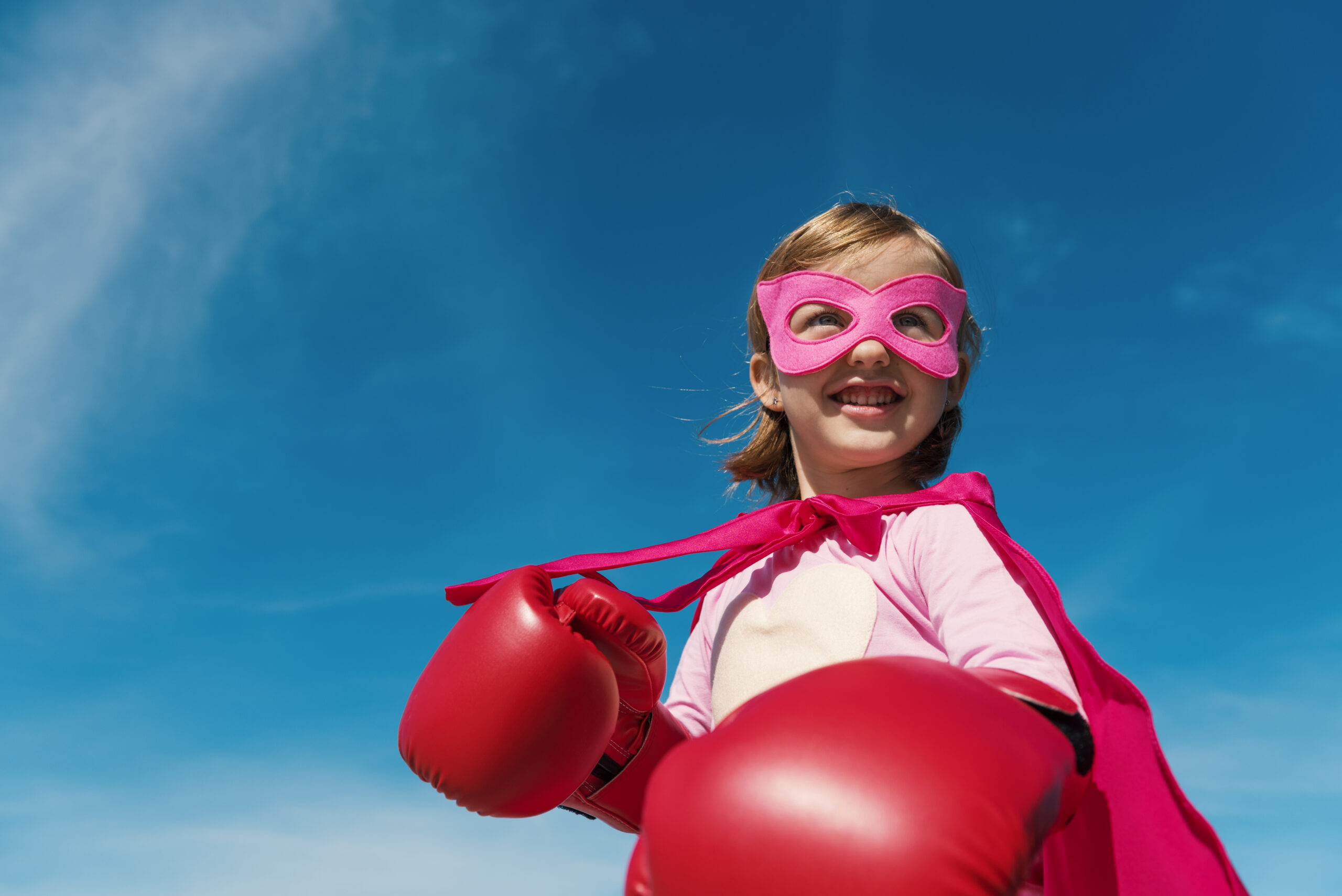 Petite fille mignonne jouant au super-héros avec un masque et une cape roses. Porte des gants de boxe, prête à en découvre avec le reste du monde.