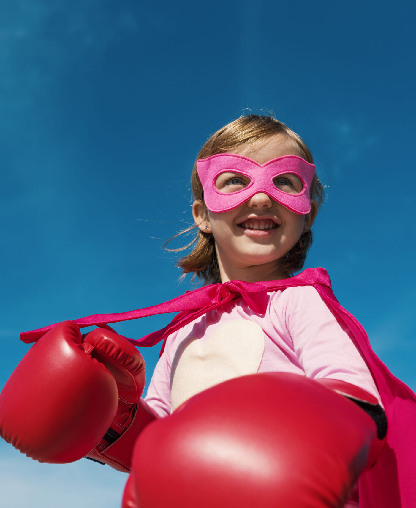 Petite fille mignonne jouant au super-héros avec un masque et une cape roses. Porte des gants de boxe, prête à en découvre avec le reste du monde.